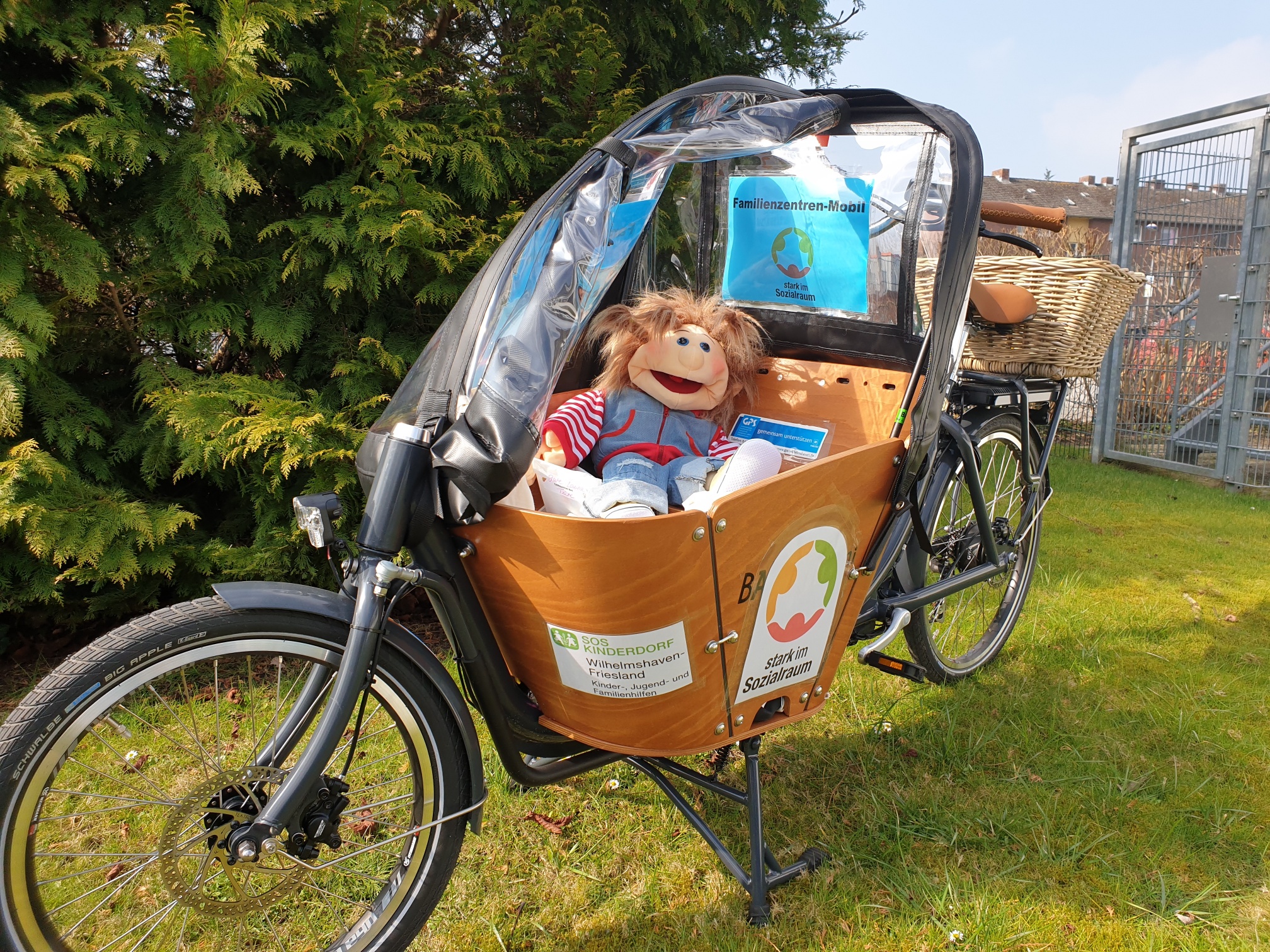 Ein Lastenfahrrad mit Logos und Aufkleber mit einer Puppe darin