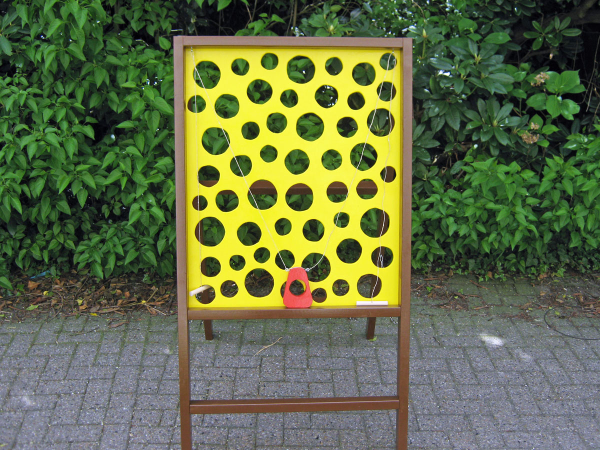 Ein Spielgerät. Eine Tafel mit vielen Löchern. Die Tafel besteht aus Holz und im inneren ist es wie Käse gelb angemalt. Ein Spiel mit Kugeln und einem Schieber