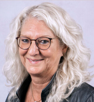 Edith Faiß. Eine Frau mit einer Brille und langen weißen Haaren. Sie trägt eine Kette