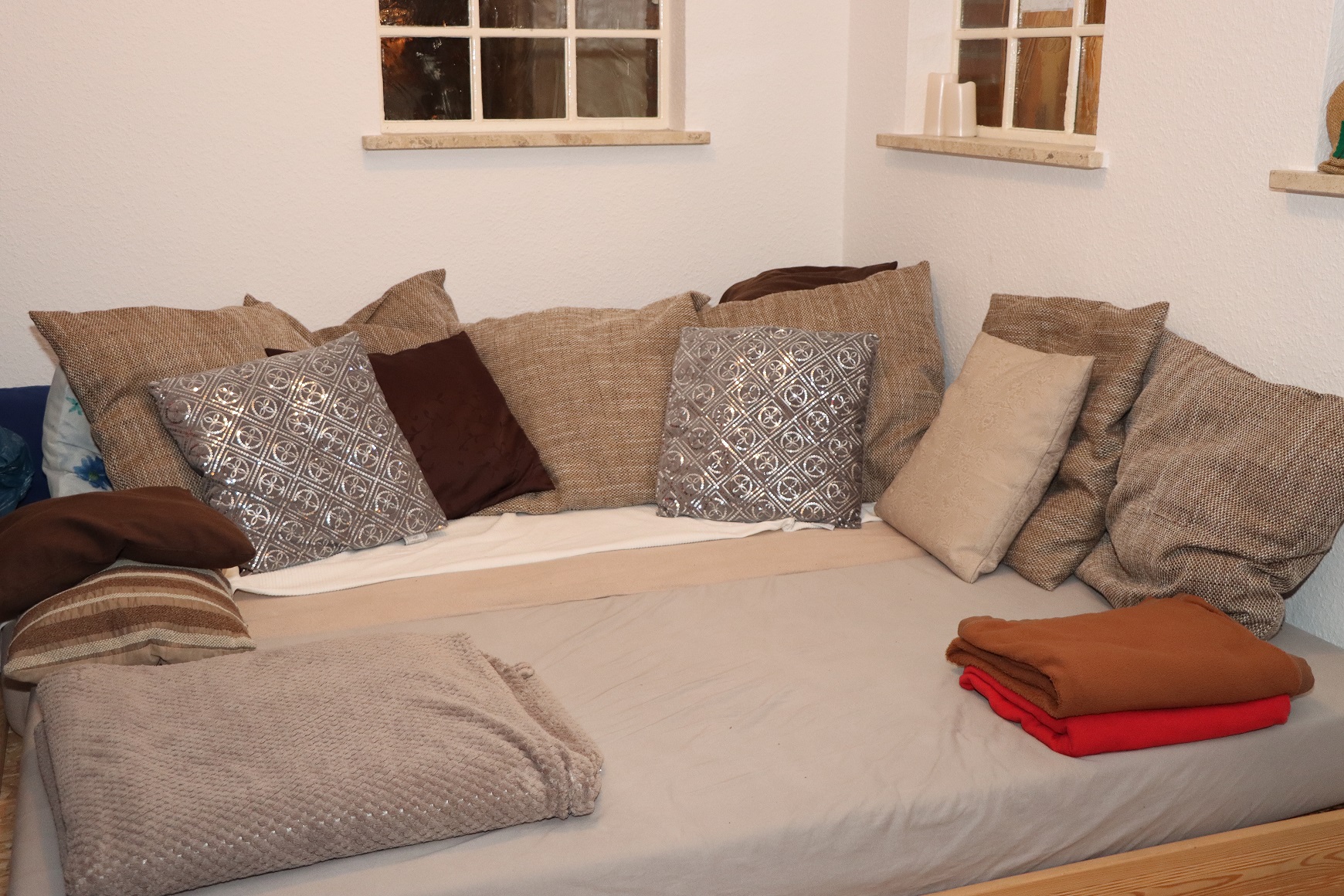 Ein Schlafplatz mit vielen Kissen und zwei Decken in einem Wohnzimmer