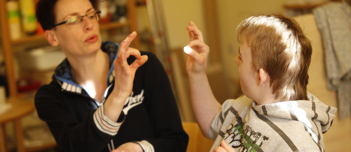 Pädagogin spricht in Gebärdensprache mit jungen Mann mit Behinderung
