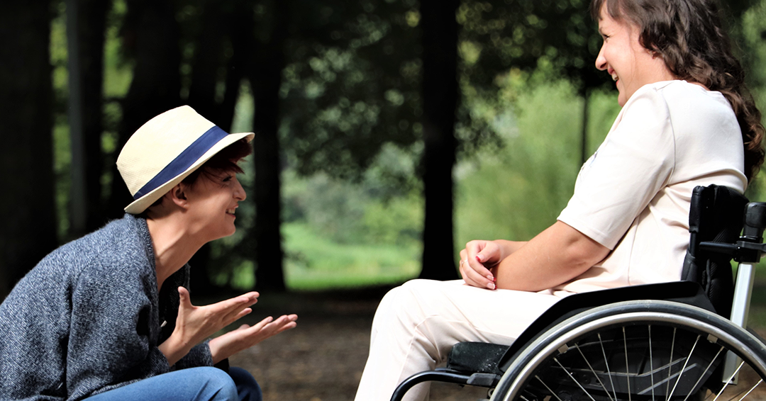 Fröhliche junge Frau mit Rollstuhlfahrerin im Gespräch
