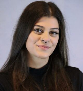 Alisha Bencka. Eine lächelnde Frau mit schwarzen langen Haaren. Sie trägt ein Piercing