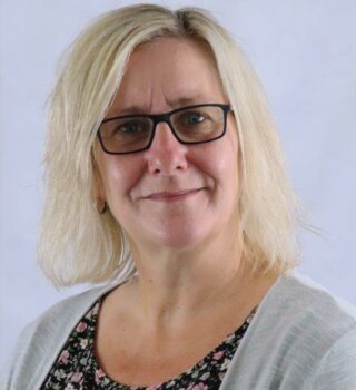 Andrea Theilen. Eine Frau mit schulterlangen blonden Haaren und eine Brille. Sie trägt Ohrringe