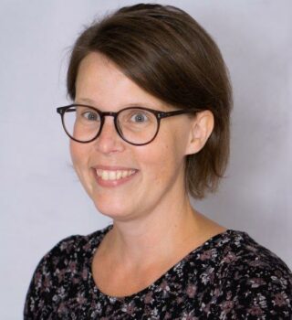 Nina Dunckel. Eine lächelnde Frau mit einer Brille und kurzen dunklen Haaren