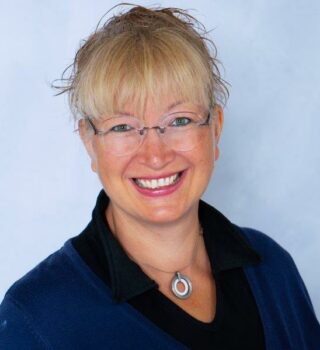 Bianca Rieken. Eine lächelnde Frau mit blonden langen Haaren mit Zopf und einer Brille. Sie trägt auch eine Kette
