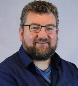Stephan Dulle. Ein lächelnder Mann mit kurzen grauen Haaren und Bart. Er trägt eine Brille